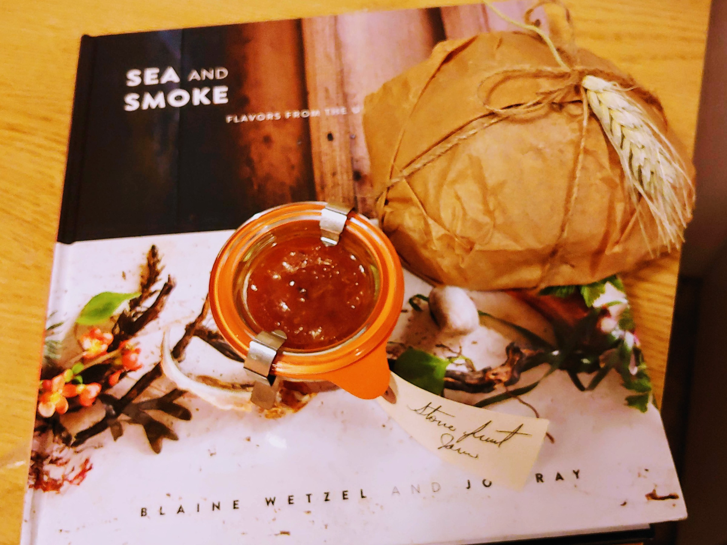 Photograph of Willows Inn cookbook, small loaf of sourdough wrapped in paper and a jar of stone fruit jam.